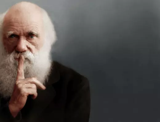 This is a picture of Darwin with his finger over his mouth like he's telling people to be quiet, and there's no text in this picture.