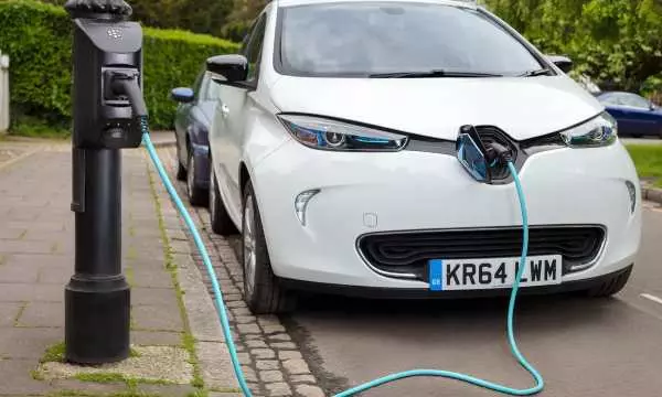 This is an image of an electric car sitting next to electric charger and it's hooked up to the car and it's charging.